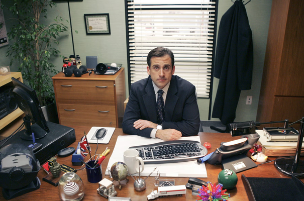 Michael Scott from The Office sat behind his cluttered desk, hands folded, looking straight at the camera